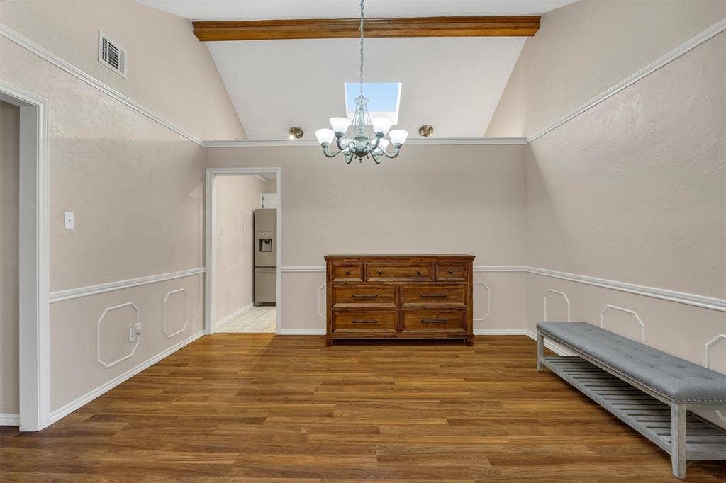 1025 Brownfield Drive, Mesquite, TX 75150 Vaulted ceiling featuring a central exposed wooden beam, skylight, and decorative crown molding, paired with wood-finish flooring and wainscoting