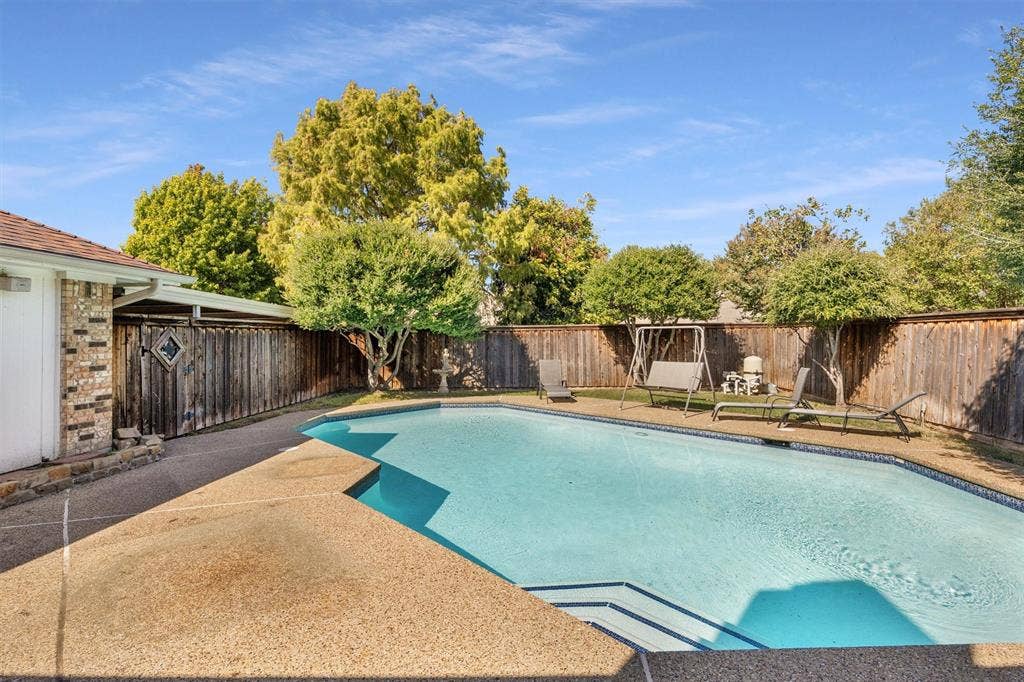 1025 Brownfield Drive, Mesquite, TX 75150 In-ground swimming pool featuring a textured concrete deck, tiered entry steps, privacy wood fencing, and mature landscaping