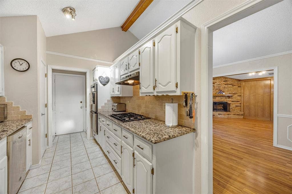 1025 Brownfield Drive, Mesquite, TX 75150 Kitchen featuring white cabinetry, stone-patterned countertops, tile flooring, built-in double wall ovens, and vaulted ceilings