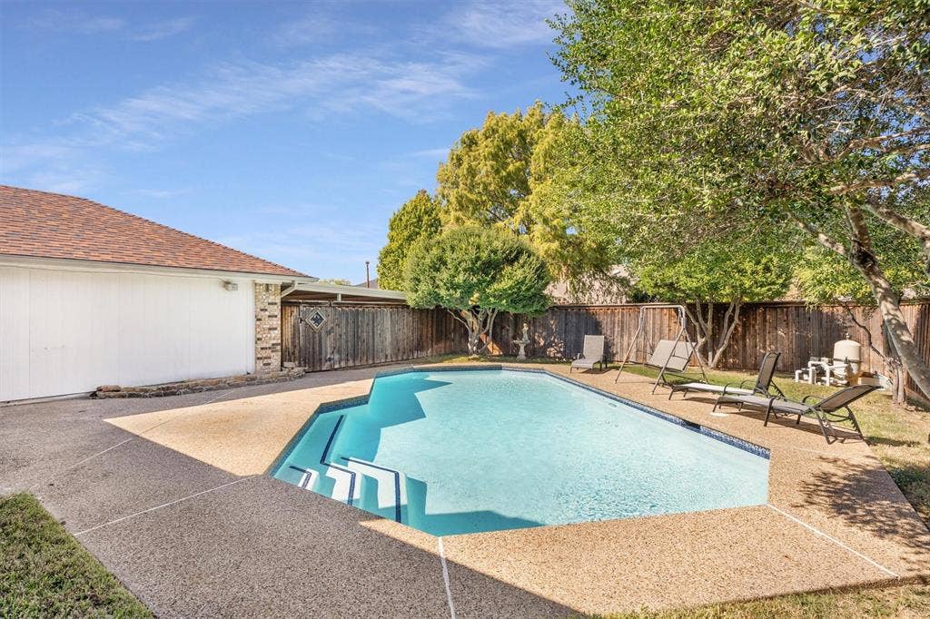 1025 Brownfield Drive, Mesquite, TX 75150 In-ground swimming pool featuring a multi-level entry, exposed aggregate pool decking, perimeter wood fencing, and mature trees