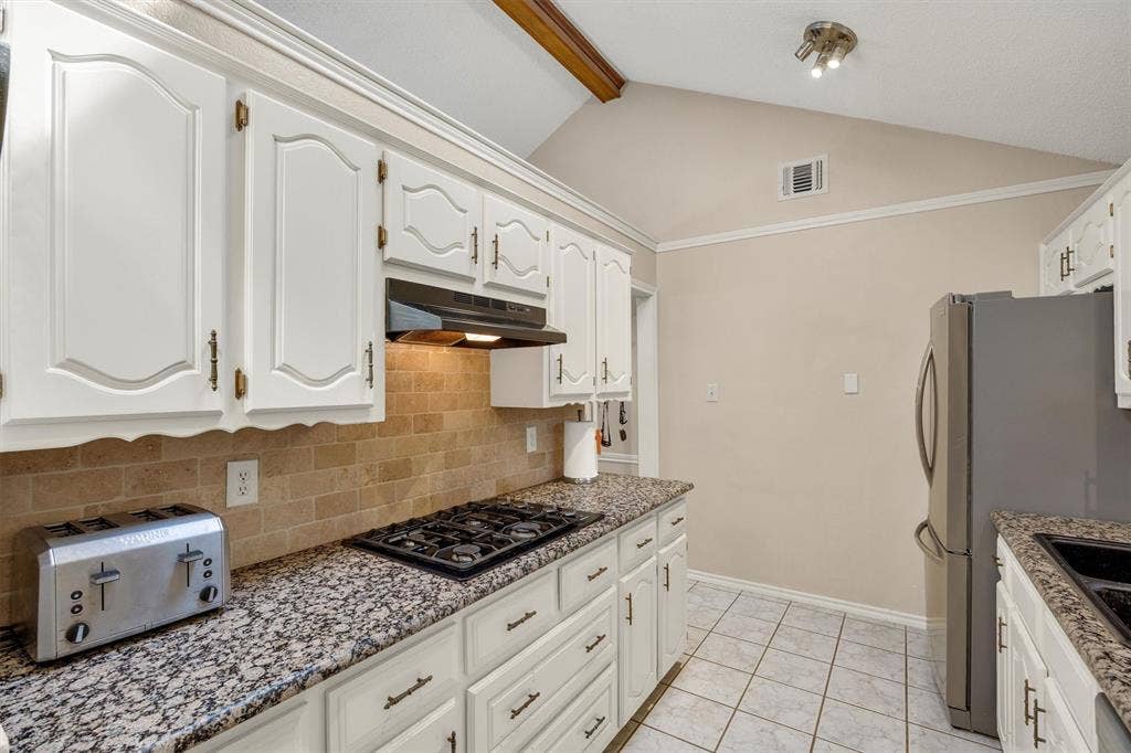 1025 Brownfield Drive, Mesquite, TX 75150 Kitchen featuring vaulted ceilings, white cabinetry with metallic hardware, stone-finish countertops, tiled backsplash, and stainless steel appliances