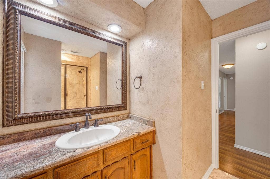 1025 Brownfield Drive, Mesquite, TX 75150 Vanity featuring a stone-surface countertop, integrated oval sink, and wood cabinetry, paired with a framed mirror, recessed lighting, and metallic wall-mounted hardware
