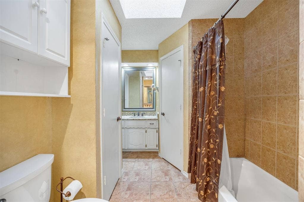 1025 Brownfield Drive, Mesquite, TX 75150 Bathroom featuring a skylight, tile flooring, vanity with stone-surface countertop, and a tiled shower surround