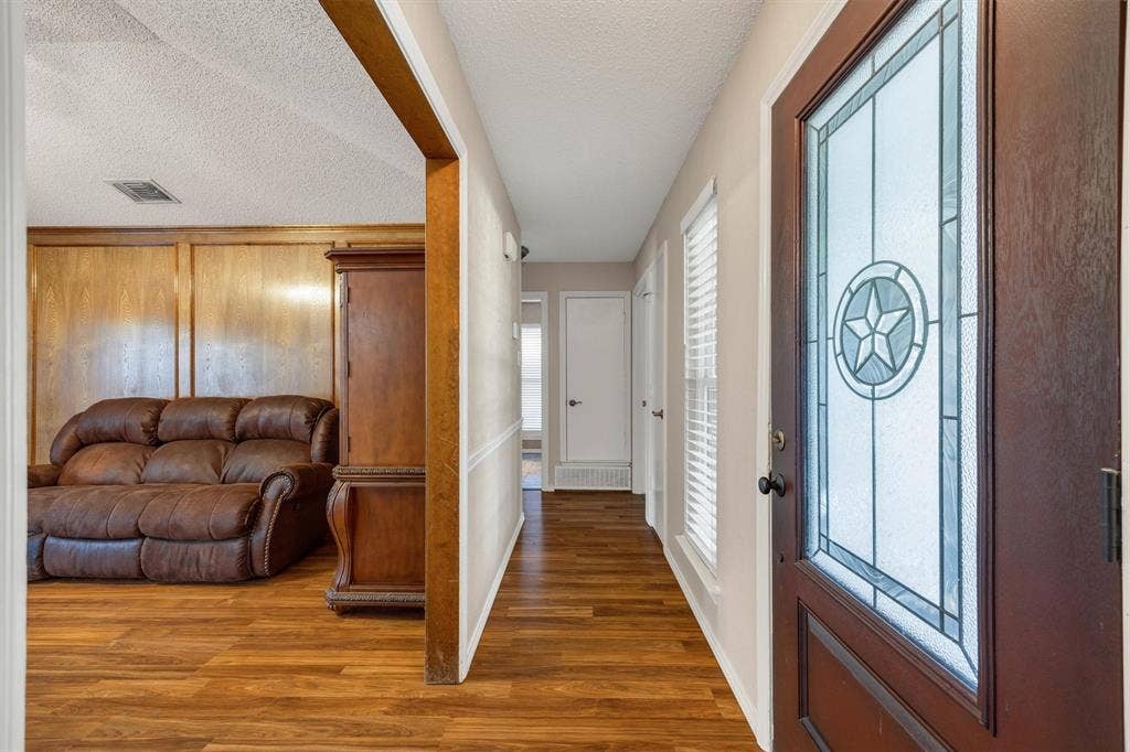 1025 Brownfield Drive, Mesquite, TX 75150 Entryway featuring a dark wood-finish door with decorative leaded glass paneling, wood-finish flooring, wood-paneled walls, and chair rail molding
