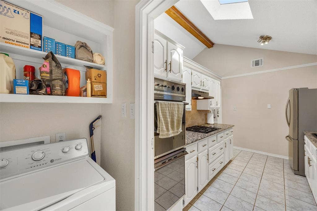 1025 Brownfield Drive, Mesquite, TX 75150 Kitchen featuring white cabinetry, stone-surface countertops, built-in dual wall ovens, and tile flooring, with a skylight and wood-beam ceiling detailing