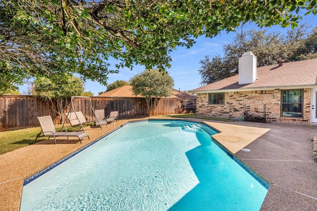 1025 Brownfield Drive, Mesquite, TX 75150 Backyard featuring an in-ground swimming pool, aggregate decking, brick exterior cladding, a masonry chimney, and perimeter wood fencing