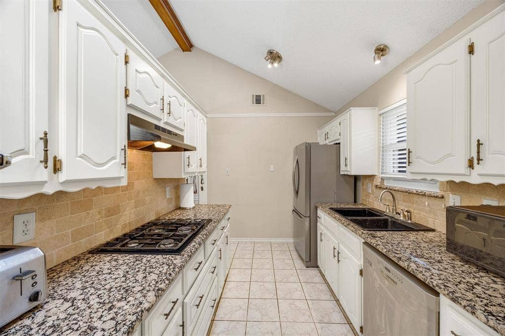 1025 Brownfield Drive, Mesquite, TX 75150 Kitchen featuring white cabinetry, stone-finish countertops, tile backsplash, stainless steel appliances, and vaulted ceilings