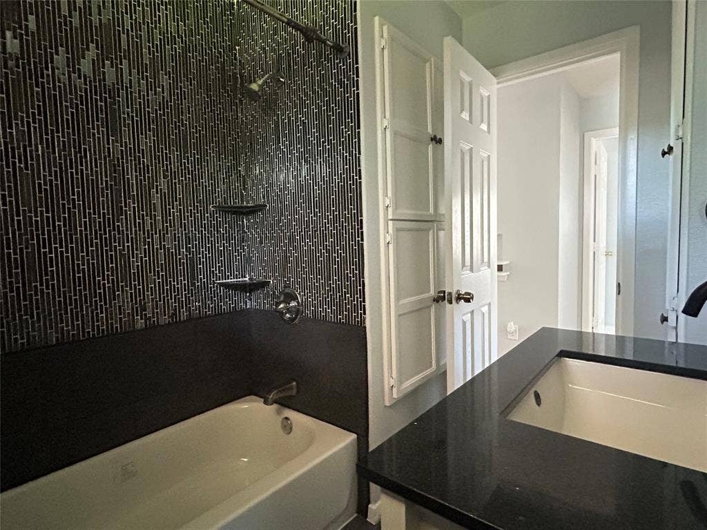 3136 Chatsworth Drive, Farmers Branch, TX 75234 Bathroom featuring a deep-soaking tub, floor-to-ceiling vertical mosaic tile surround, built-in shelving, dark solid-surface countertop, and an integrated rectangular basin