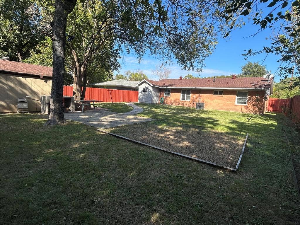 3136 Chatsworth Drive, Farmers Branch, TX 75234 Fenced backyard featuring a brick exterior, stone patio, mature trees, and a ground-level gravel area