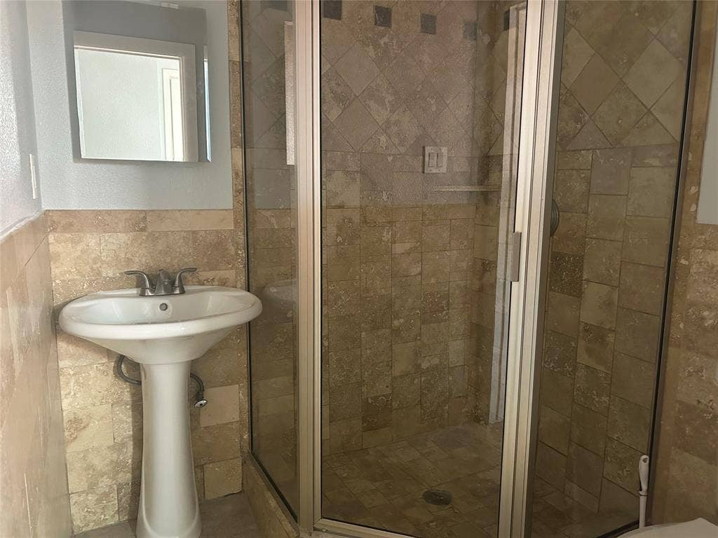 3136 Chatsworth Drive, Farmers Branch, TX 75234 Pedestal sink with chrome faucet, corner shower enclosure featuring a metal frame, and natural stone tile wall surfacing