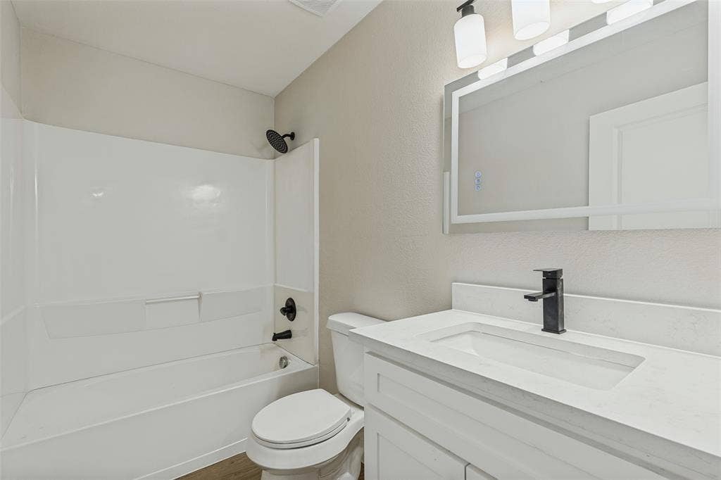 4603 Spring Garden Street, Dallas, TX 75215 Bathroom featuring a stone-composite countertop, white shaker-style vanity cabinet, matte black faucet, integrated tub and shower surround with matte black fixtures, and a LED-backlit mirror