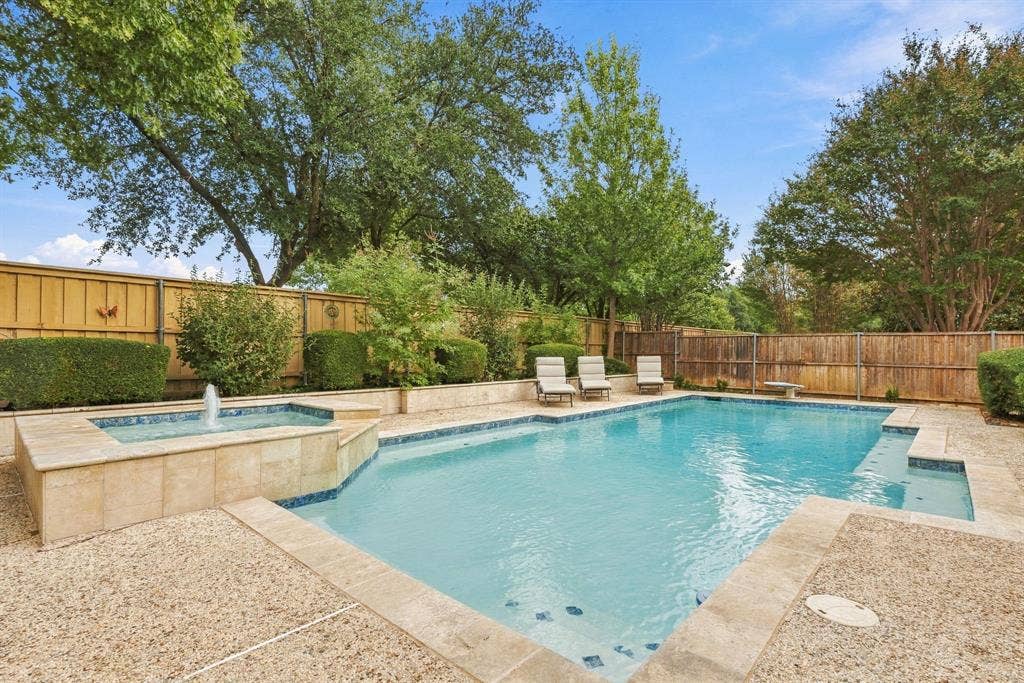 511 Clover Leaf Lane, McKinney, TX 75072 Backyard featuring an in-ground swimming pool, integrated spa with water feature, stone-finish decking, and wood privacy fencing