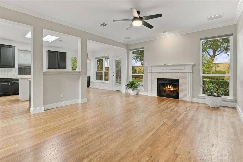 511 Clover Leaf Lane, McKinney, TX 75072 Living area featuring wood-finish flooring, a masonry fireplace with a white mantel, neutral wall tones, crown molding, and a ceiling fan with integrated lighting
