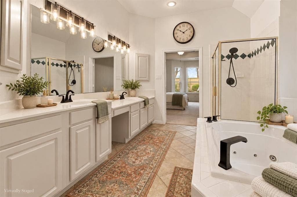 511 Clover Leaf Lane, McKinney, TX 75072 Dual-vanity cabinetry with solid-surface countertops, soaking jetted tub, enclosed glass-paneled shower with tiled inlay, and wall-mounted light fixtures