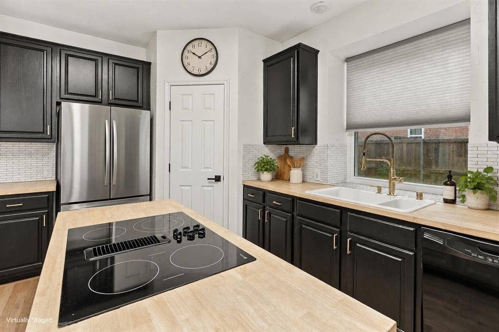 511 Clover Leaf Lane, McKinney, TX 75072 Kitchen featuring black cabinetry, wood-finish countertops, a central island with an integrated electric cooktop, stainless steel refrigerator, and white subway tile backsplash
