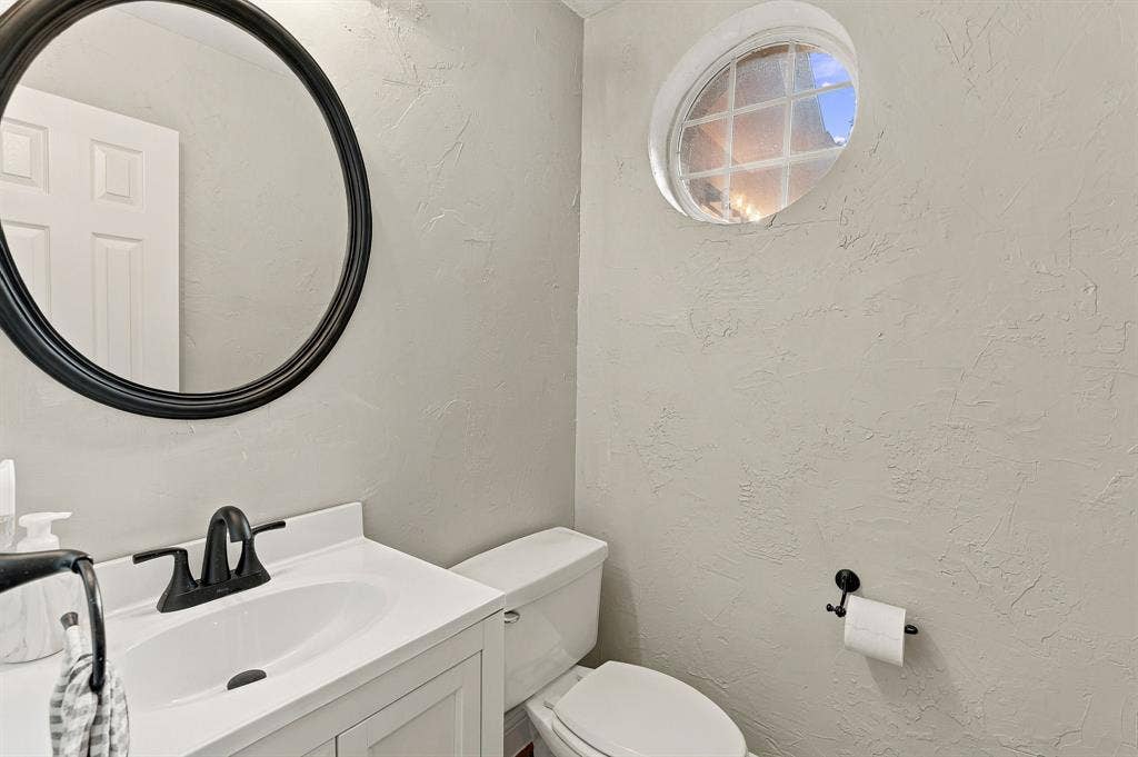 511 Clover Leaf Lane, McKinney, TX 75072 Bathroom featuring a white vanity cabinet, matte black faucet, circular black-framed mirror, and a decorative oval window with muntins