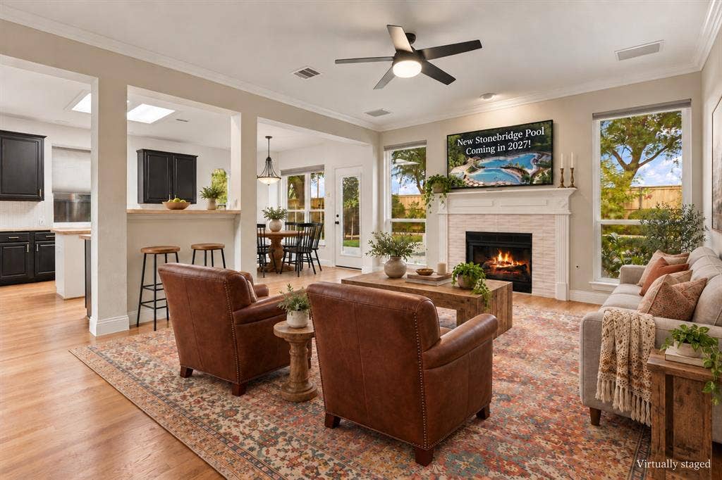 511 Clover Leaf Lane, McKinney, TX 75072 Living area featuring wood-finish flooring, fireplace with a mantle and tiled surround, crown molding, ceiling fan with integrated lighting, and multiple tall windows
