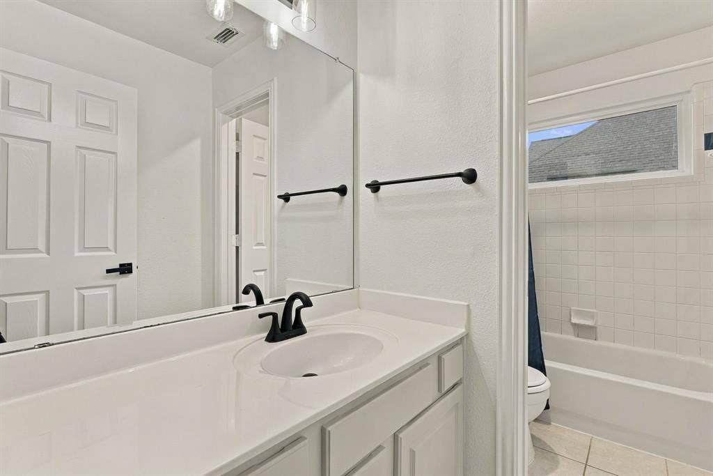 511 Clover Leaf Lane, McKinney, TX 75072 Bathroom vanity featuring a solid surface countertop, undermount sink, matte black faucet hardware, and a wall-to-wall mirror with multi-bulb overhead lighting