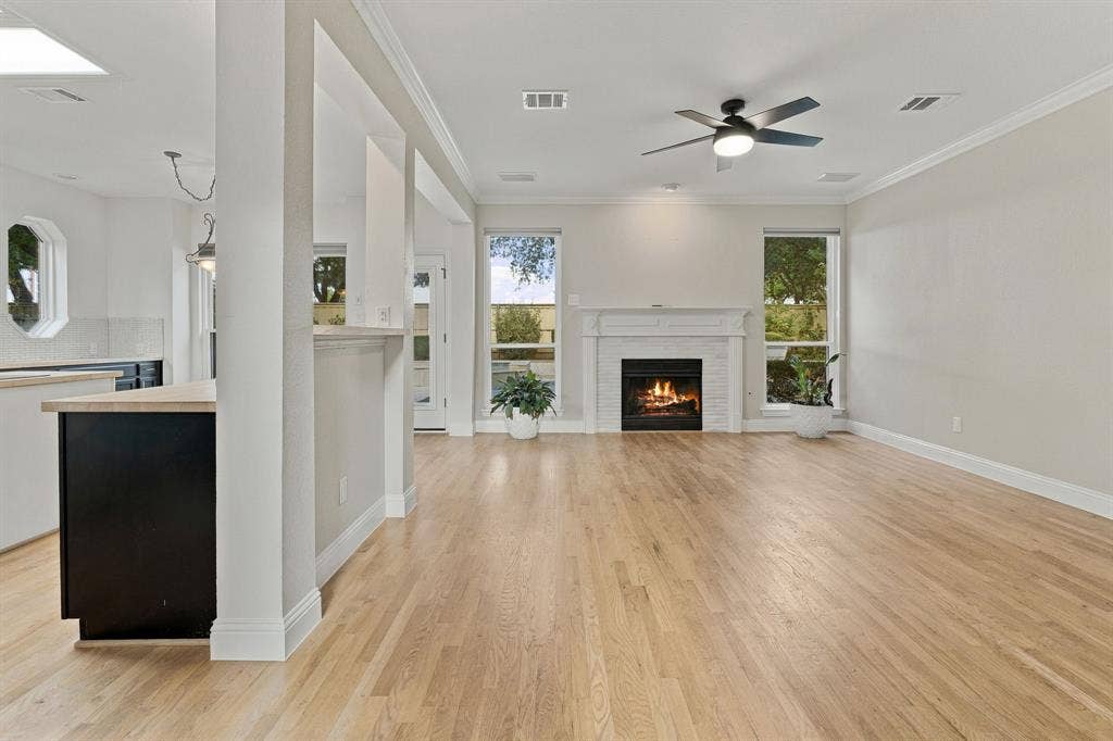 511 Clover Leaf Lane, McKinney, TX 75072 Living area featuring wood-finish flooring, a white brick fireplace with a decorative mantel, multiple floor-to-ceiling windows, and a ceiling fan with integrated lighting