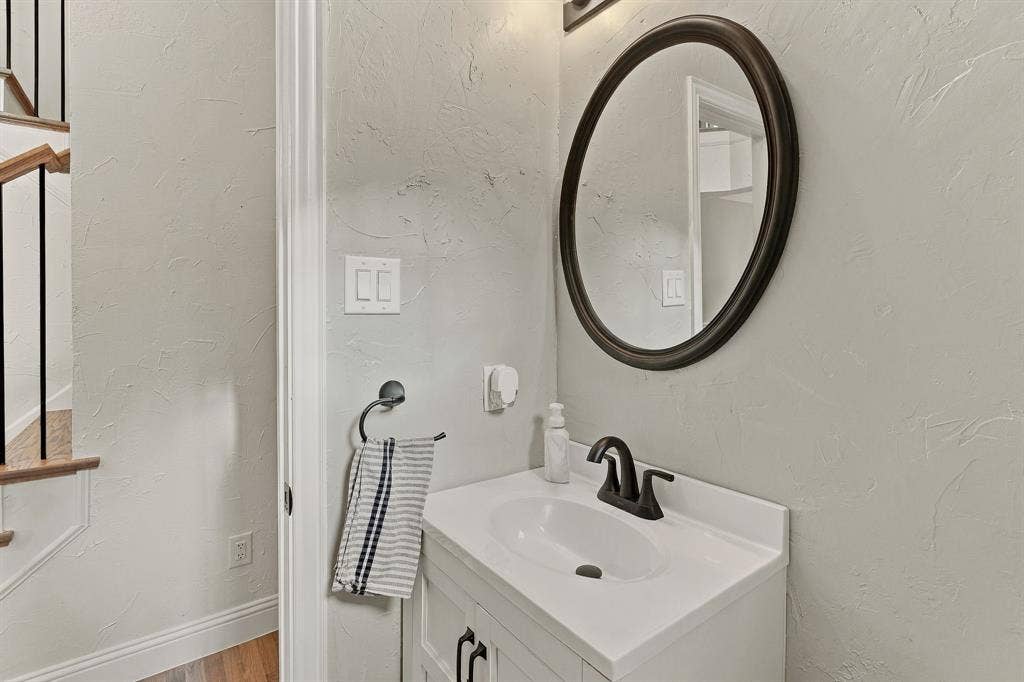 511 Clover Leaf Lane, McKinney, TX 75072 White vanity featuring a rectangular basin, matte black faucet, oval-framed mirror, and textured wall finish
