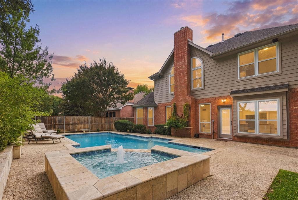 511 Clover Leaf Lane, McKinney, TX 75072 Rear exterior featuring a brick and horizontal siding facade, a custom swimming pool with an integrated raised spa, a fountain feature, and a textured concrete patio