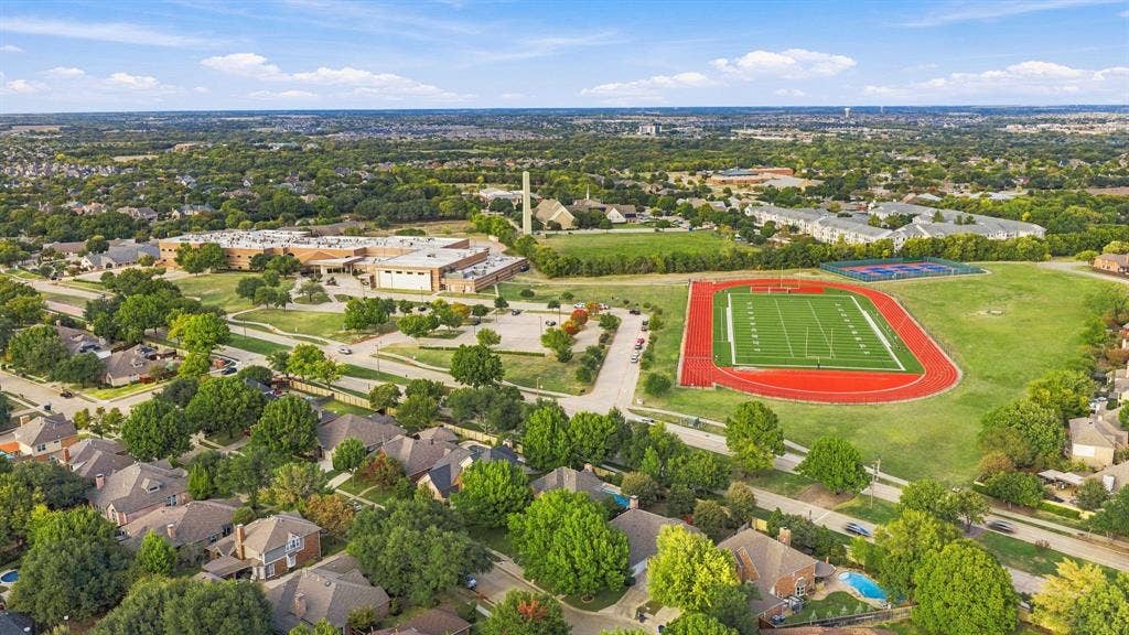 511 Clover Leaf Lane, McKinney, TX 75072 Aerial perspective of a residential neighborhood featuring established tree canopy, paved thoroughfares, athletic field with running track, and hardscaped courts