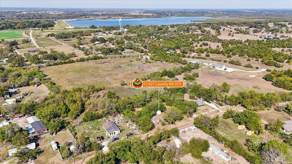 Aerial perspective of expansive acreage featuring mature trees, open grassy areas, and proximity to a large body of water