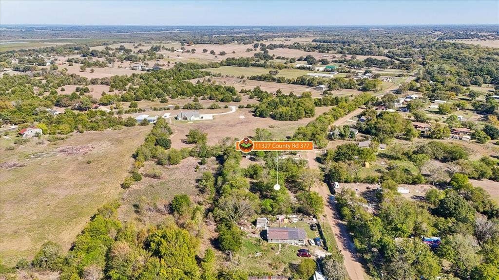 Aerial view of expansive rural acreage featuring mature trees, open pasture, and a paved road frontage