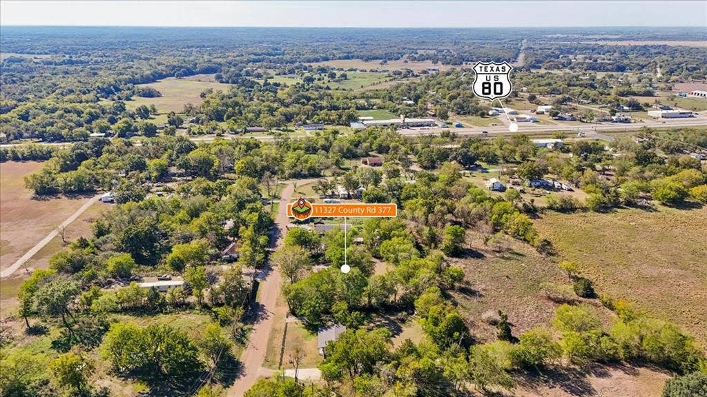 Aerial perspective of a multi-acre property featuring mature tree clusters, open pasture land, and established road access near US-80