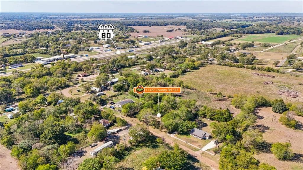 Aerial perspective of expansive acreage featuring mature trees, open pastureland, and a single-story structure with a paved driveway