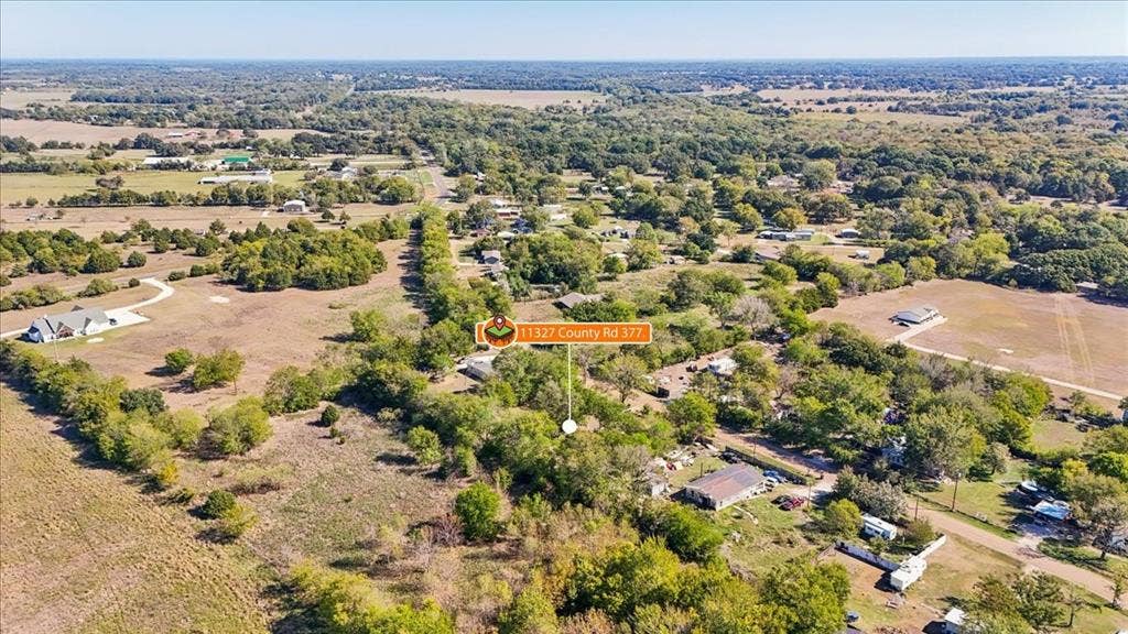 Aerial perspective of expansive acreage featuring mature trees, open pastureland, and established rural surroundings