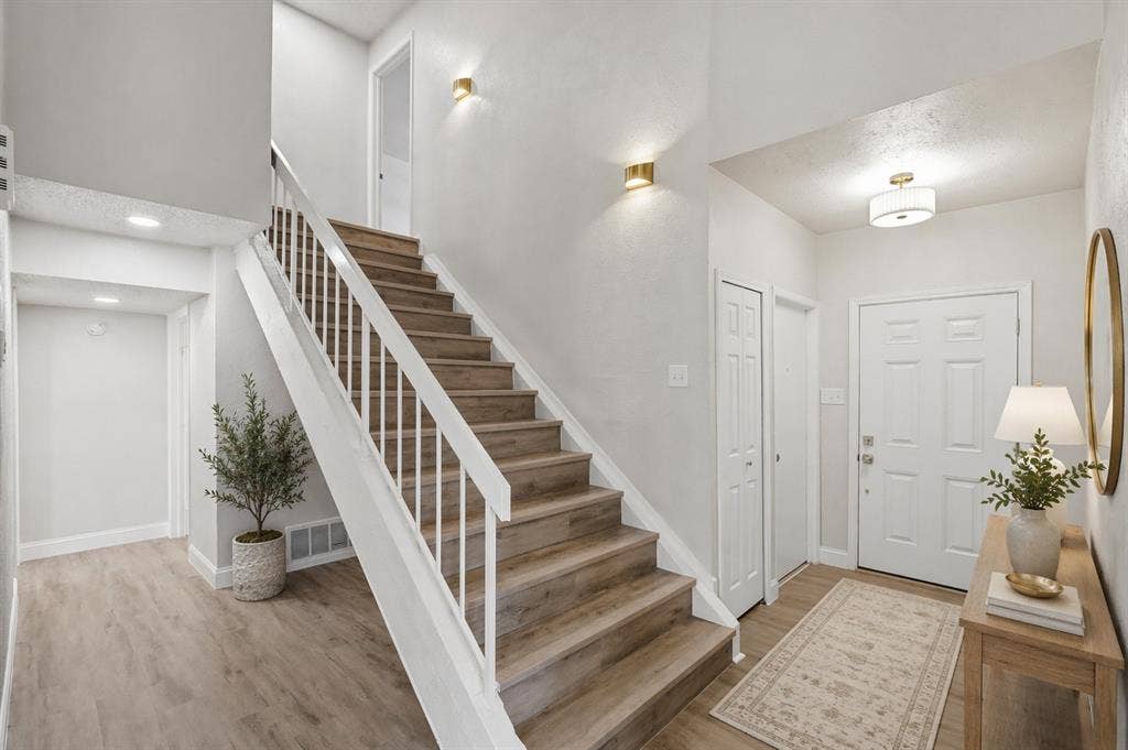 5514 Round Rock Road, Garland, TX 75044 Entryway featuring wood-finish flooring, a staircase with white metal railings, recessed ceiling lighting, wall-mounted metallic sconces, and a panelled front door