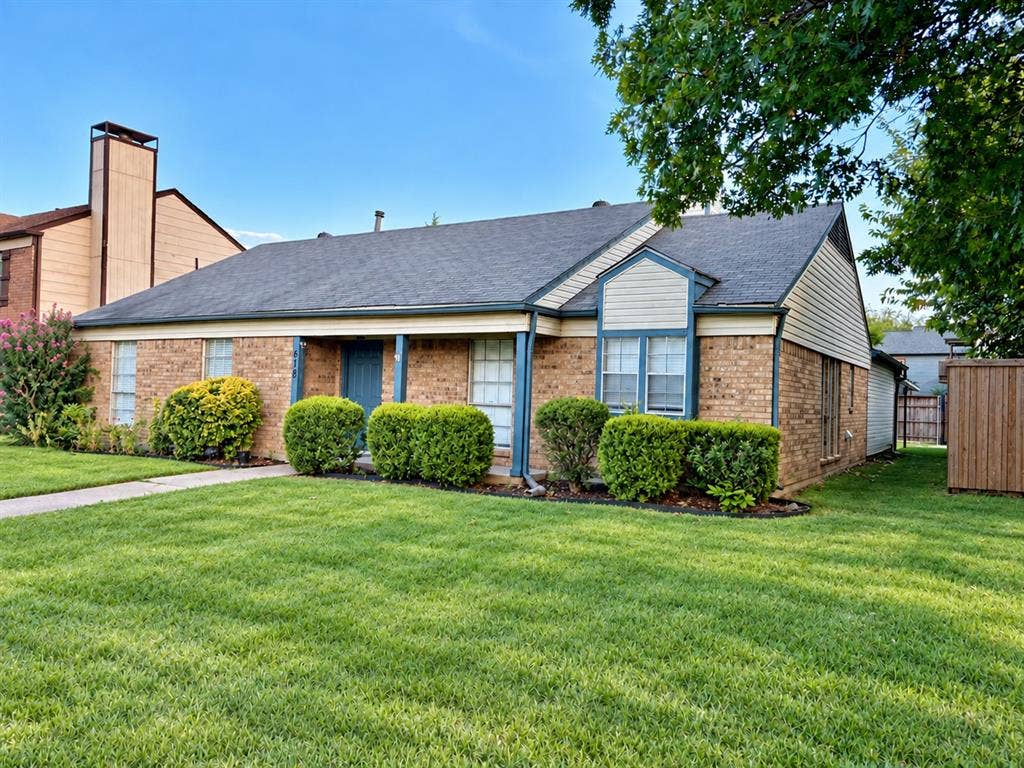 618 Pyramid Drive, Garland, TX 75040 Single-story brick exterior featuring a multi-gabled roofline, covered front entryway, paneled siding accents, and a front lawn with established landscaping