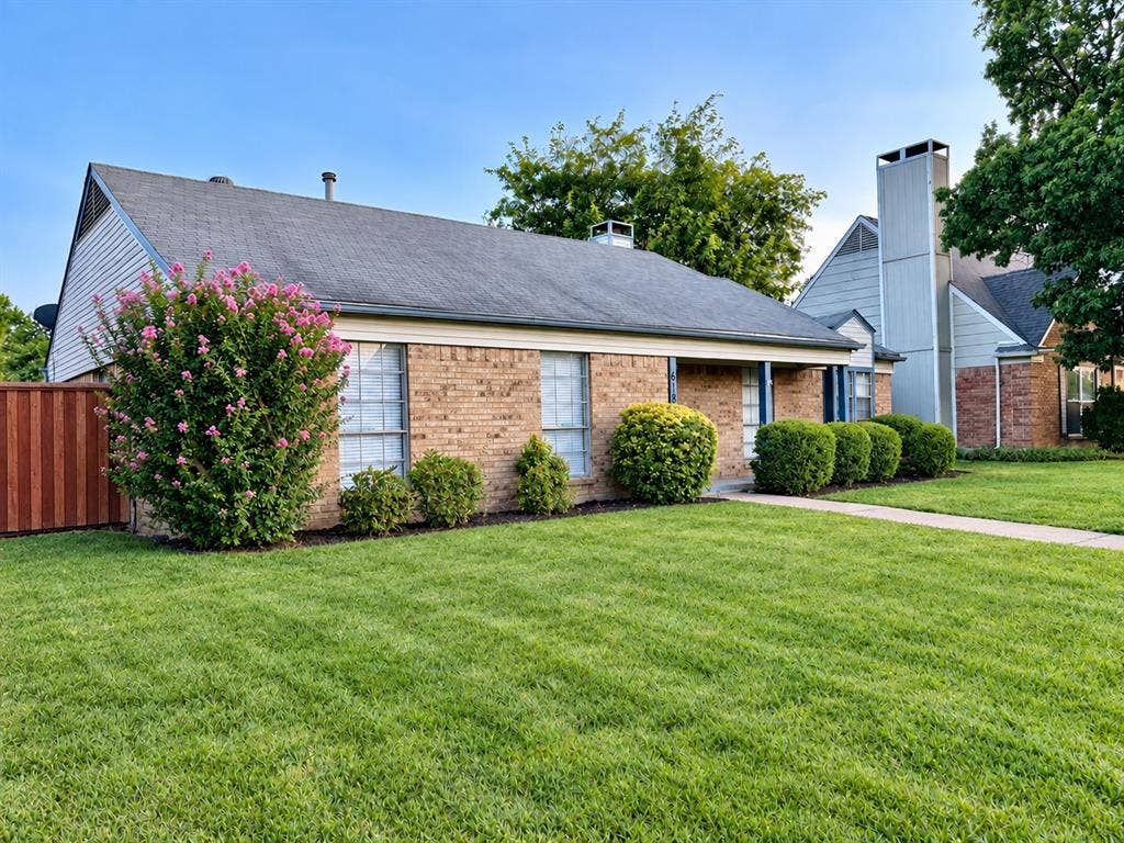 618 Pyramid Drive, Garland, TX 75040 Brick exterior featuring a multi-gabled roofline, prominent chimney, wood-tone fencing, and manicured landscaping