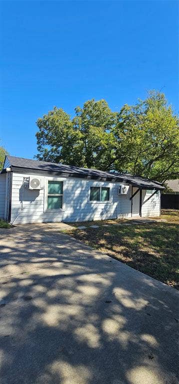 Exterior featuring white horizontal siding, dark roofing, concrete driveway, and wall-mounted HVAC units