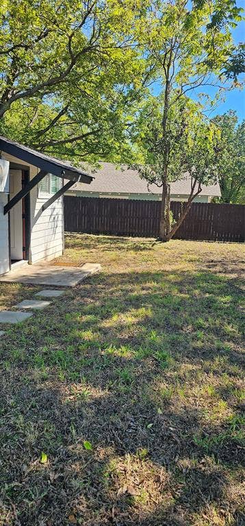 Exterior backyard featuring a concrete patio, stone paver walkway, mature trees, and a wood privacy fence