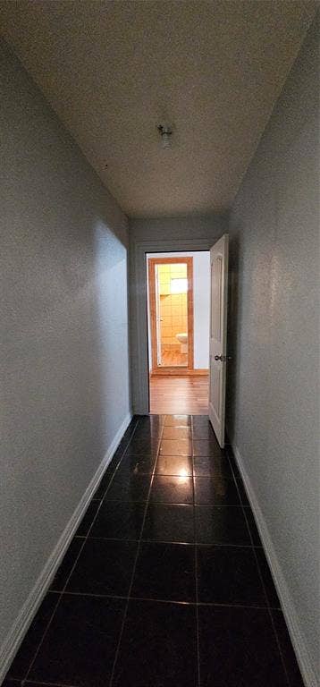 Hallway featuring dark square tile flooring, neutral painted walls, and a single-panel interior door