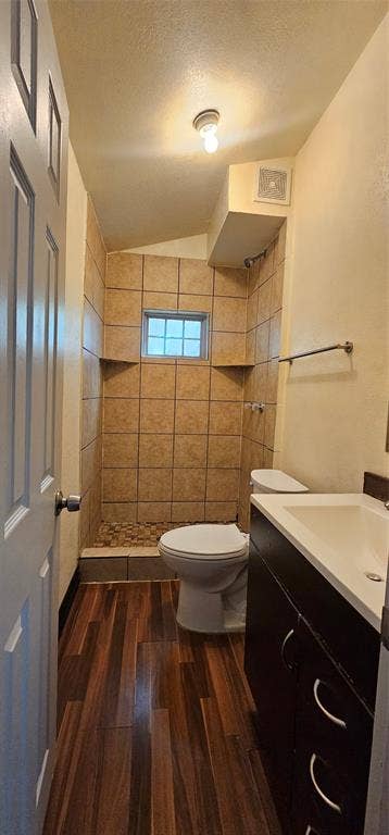 Bathroom featuring a walk-in shower with tile surround and stone flooring, wood-finish flooring, dark cabinetry with a white countertop, and a recessed window
