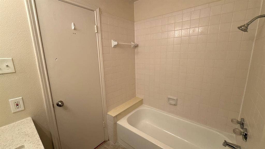 Bathtub featuring white square tile surround, integrated tiled ledge, and chrome-finish fixtures
