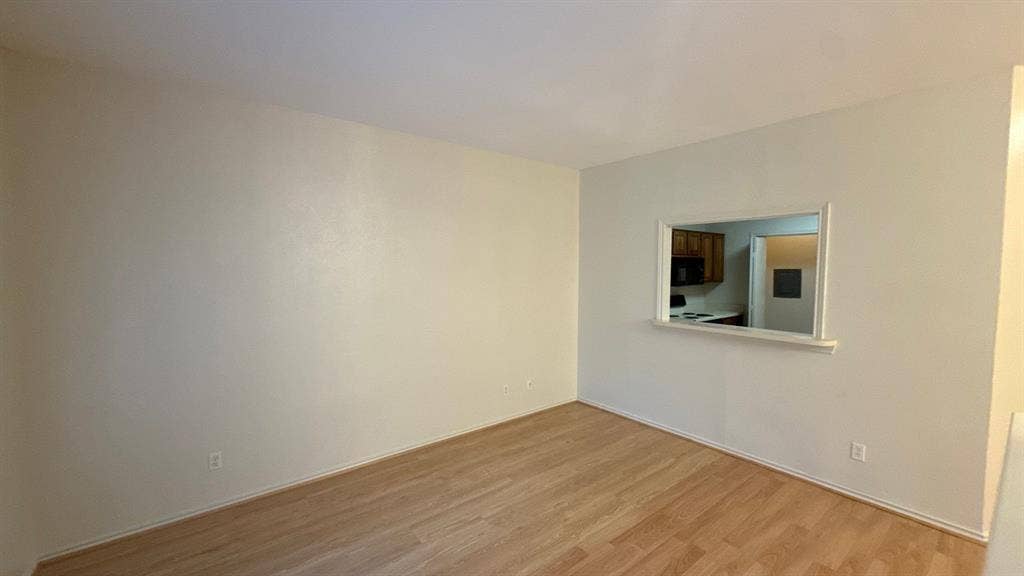 Neutral-toned interior space featuring wood-finish flooring and a rectangular pass-through window with a trim surround