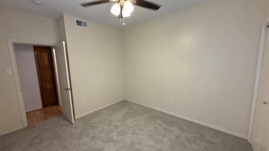 Neutral-toned room with plush carpeting, ceiling fan with light fixture, and wooden paneled door
