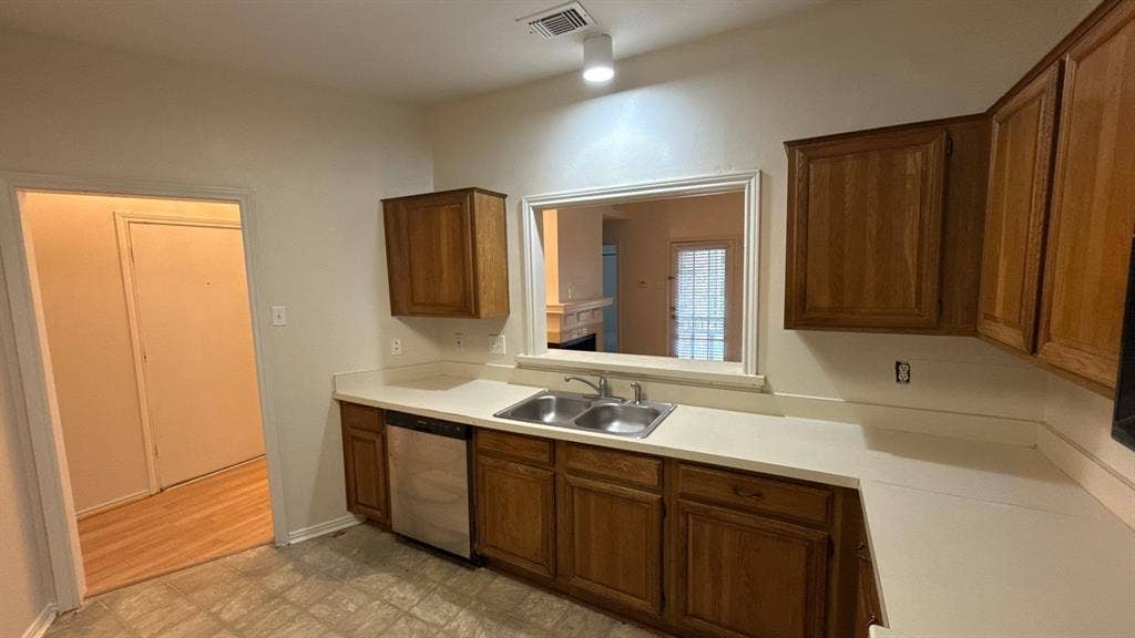 Kitchen featuring wood cabinetry, solid-surface countertops, dual-basin stainless steel sink, and stainless steel dishwasher