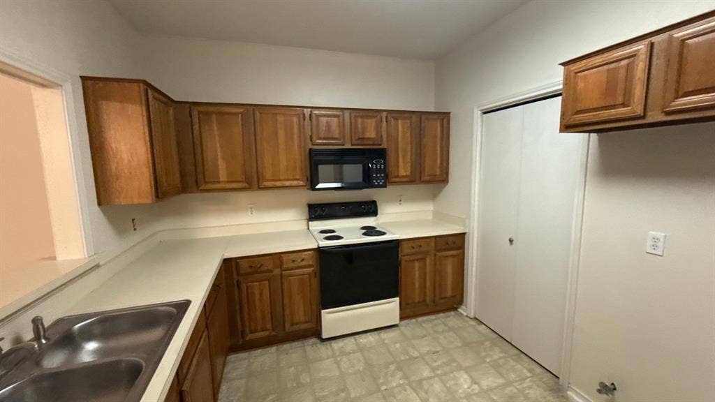 Kitchen featuring wood cabinetry, solid-surface countertops, dual-basin stainless steel sink, over-the-range microwave, and pantry closet