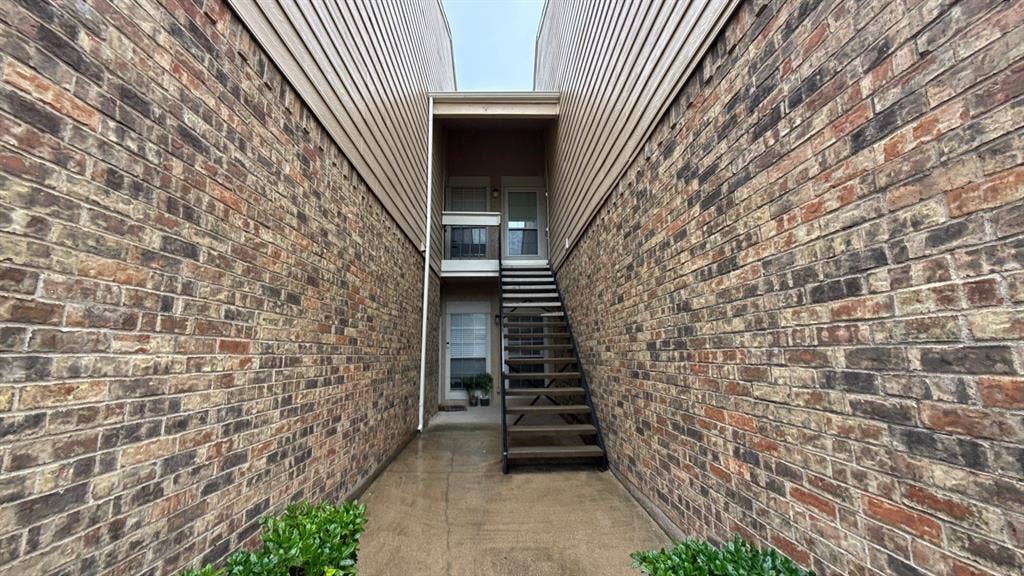 Exterior facade featuring multi-tonal brick masonry, horizontal siding, and a metal staircase