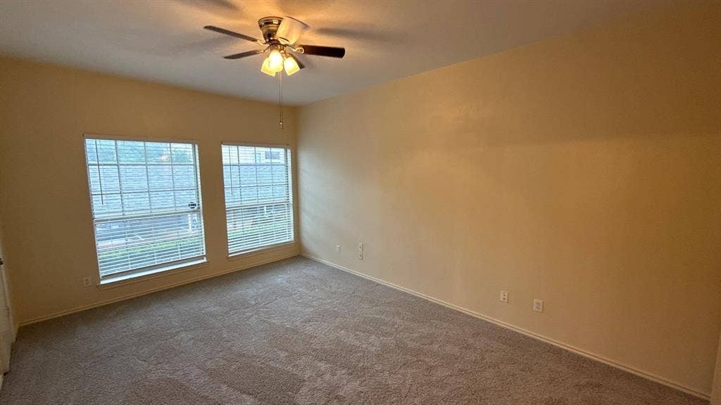 Neutral-toned interior space featuring wall-to-wall carpeting, two dual-pane windows with grid detailing, and a ceiling-mounted light fixture with a fan