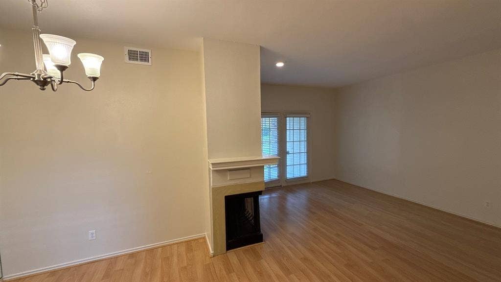 Open-concept interior featuring wood-finish flooring, a centrally positioned fireplace with a decorative mantel, a multi-arm chandelier, and glass-paned double doors