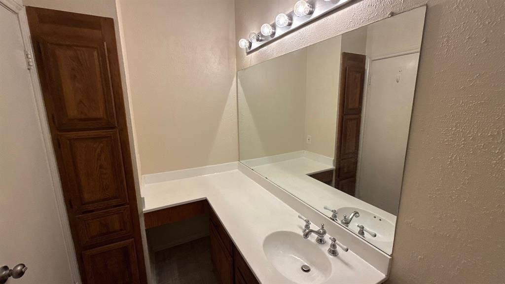 Bathroom vanity featuring wood-finish cabinetry, a white countertop with an integrated oval sink, a large wall-mounted mirror, and multi-bulb strip lighting