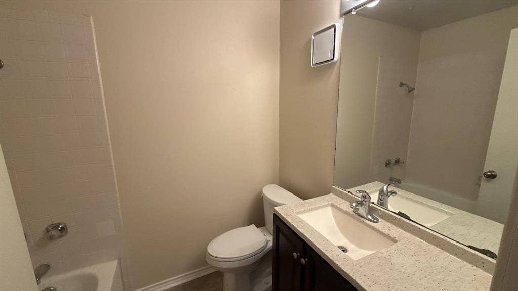 Bathroom featuring a vanity with a light-toned speckled countertop, an integrated basin, a large wall-mounted mirror, and a tub-shower combination with tile surround