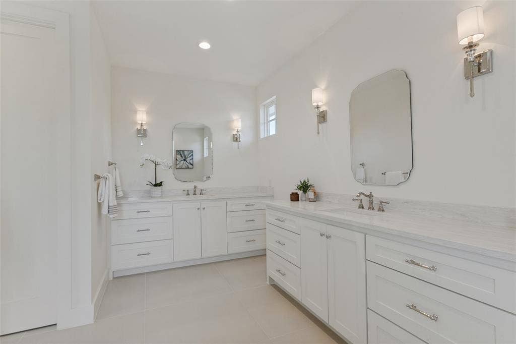 304 S Weatherred Drive, Richardson, TX 75080 Dual white cabinetry with stone countertops, undermount sinks, polished metal fixtures, and arched wall-mounted mirrors