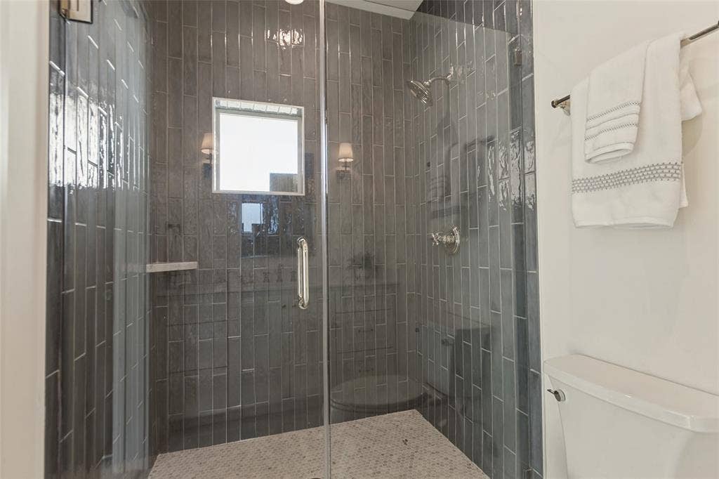 304 S Weatherred Drive, Richardson, TX 75080 Walk-in shower featuring vertical subway tile surround, frameless glass door, wall-mounted rainfall showerhead, and pebble-style stone flooring